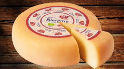 Ein ganzer Laib Bierkäse mit einem herausgeschnittenen Keil, der auf einer Holzplatte ausgestellt ist.