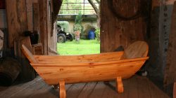 Eine Holzbadewanne steht auf einem rustikalen Holzboden in einer Scheune mit Blick auf einen grasbewachsenen Hof.