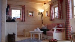 Gemütliches Wohnzimmer aus Holz mit rosafarbenem Sofa, karierten Vorhängen, einem Teppich und einem gedeckten Tisch für Tee.