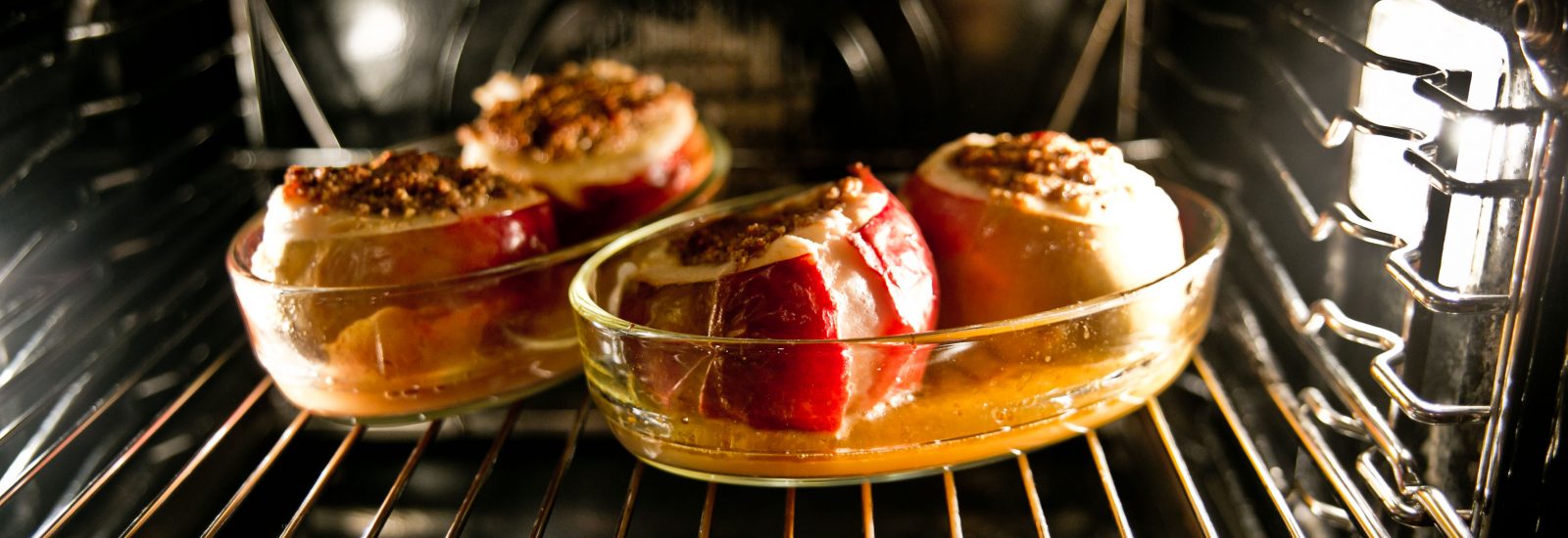 Drei gefüllte Äpfel, die in einer Glasschale im Ofen backen, wobei sich der karamellisierte Saft am Boden sammelt.