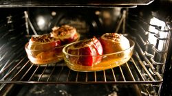 Drei gefüllte Äpfel, die in einer Glasschale im Ofen backen, wobei sich der karamellisierte Saft am Boden sammelt.