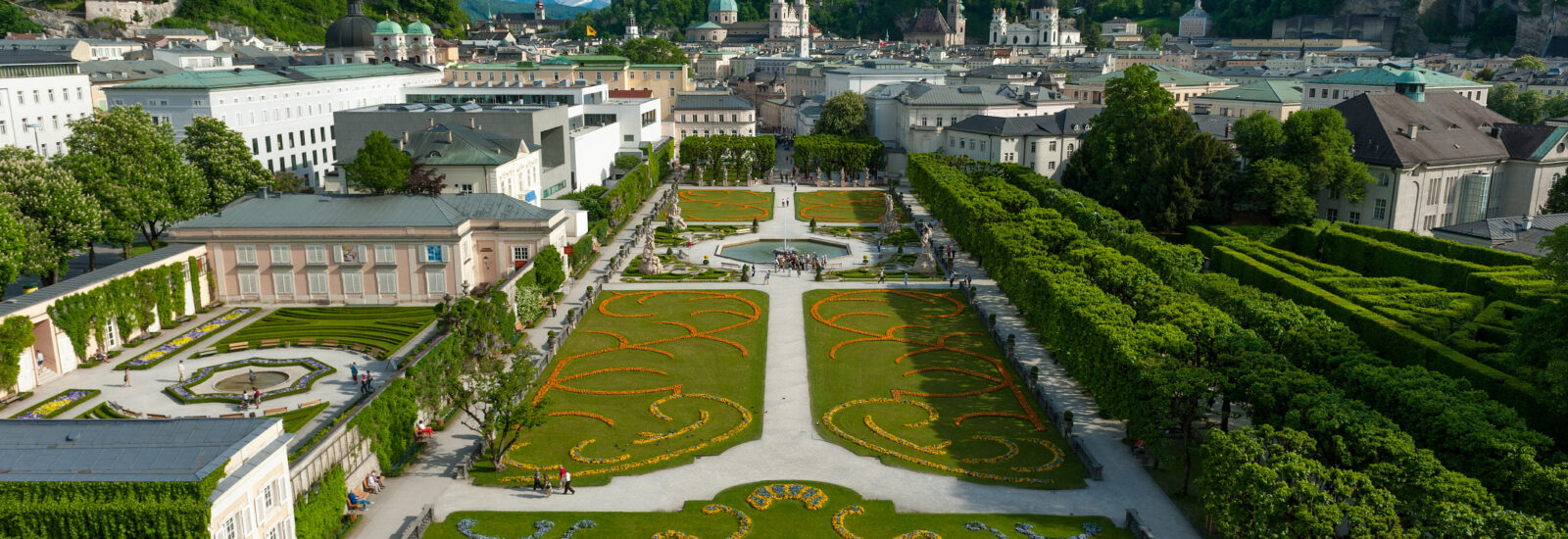 Luftaufnahme der Mirabellgärten in Salzburg mit der Festung auf dem Hügel im Hintergrund.