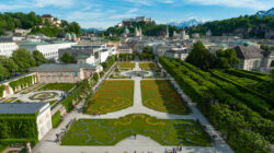 Luftaufnahme der Mirabellgärten in Salzburg mit der Festung auf dem Hügel im Hintergrund.
