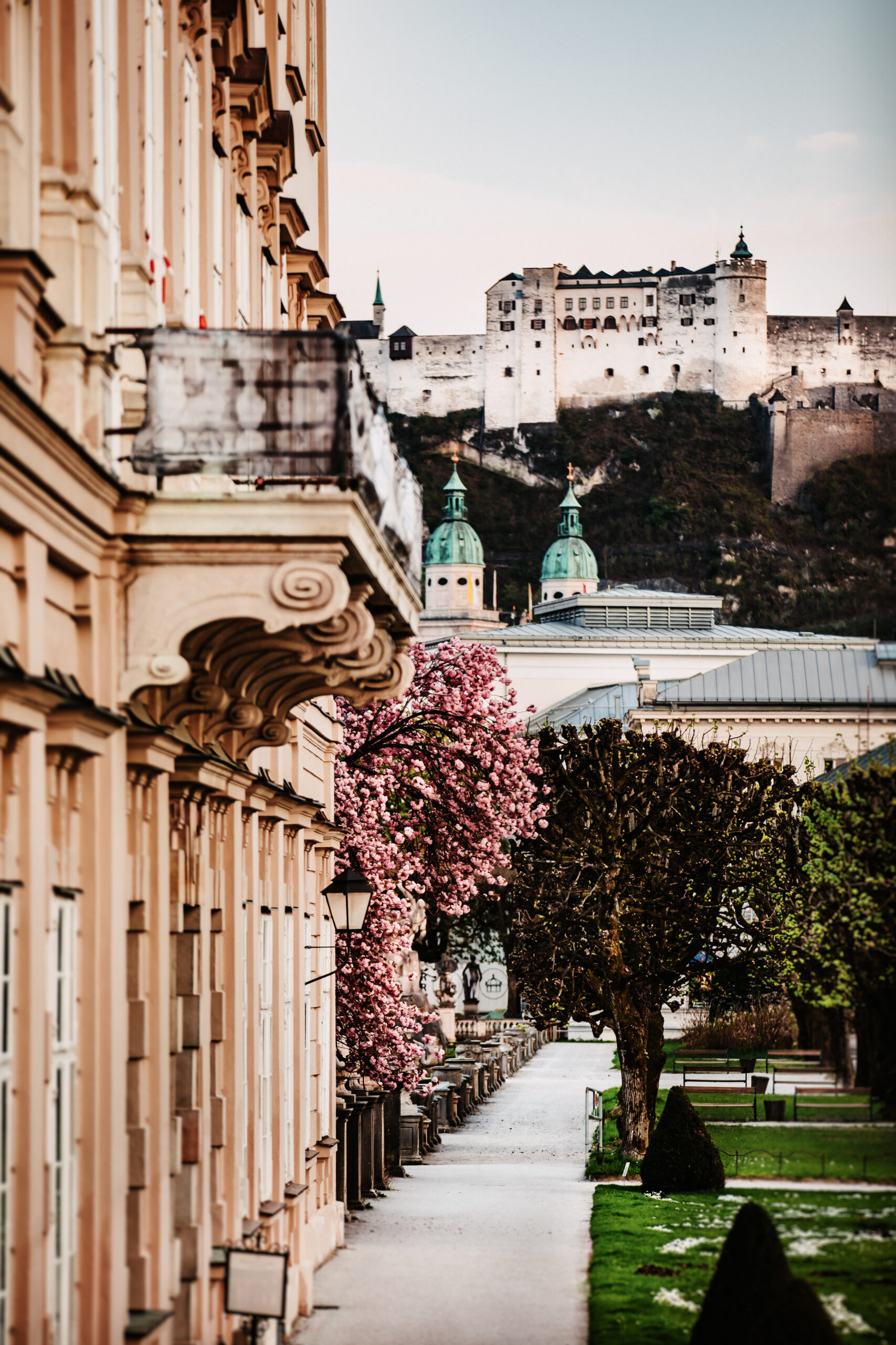 Eine von historischen Gebäuden gesäumte Straße führt zu einer in der Ferne auf einem Hügel gelegenen Burg in Österreich.