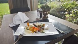 Ein Gourmet-Menü auf einem Tisch am Fenster, mit Besteck, Serviette, Salz- und Pfefferstreuer.