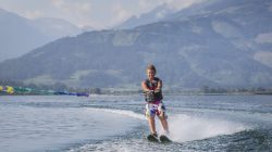 Eine Person fährt Wasserski auf einem See mit Bergen im Hintergrund unter einem klaren Himmel.