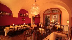 Elegantes, warm beleuchtetes Restaurant mit gewölbter Decke, kerzenbeleuchteten Tischen und einem großen Fenster mit Blick auf die Straße.