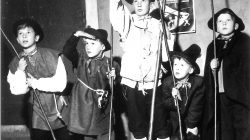 Fünf Jungen in Kostümen mit Stöcken, einer zeigt nach oben, stehen vor einem Adventsplakat an der Wand.