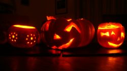 Drei leuchtende Irrlichter mit verschiedenen geschnitzten Gesichtern stehen in einem dunklen, von innen beleuchteten Raum.