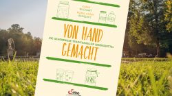 Buchdeckel Von Hand gemacht steht auf Gras mit Bäumen und einer Statue im Hintergrund an einem sonnigen Tag.