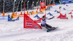 Snowboarder, der bergab fährt und ein rotes Tor in einem verschneiten Slalomkurs mit Fahnen und Flaggen umkurvt.