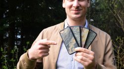 Mann im Freien, der lächelnd drei verschieden gemusterte Handyhüllen in der Hand hält und auf sie zeigt.