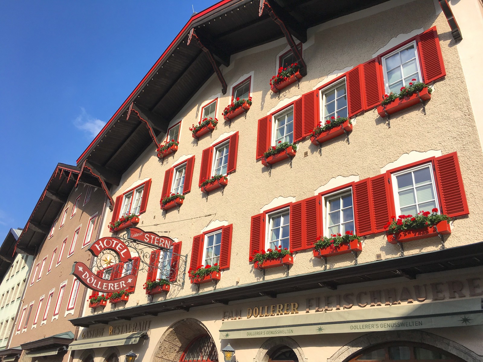 Ein Hotel mit roten Fensterläden und Blumenkästen an den Fenstern unter einem strahlend blauen Himmel.