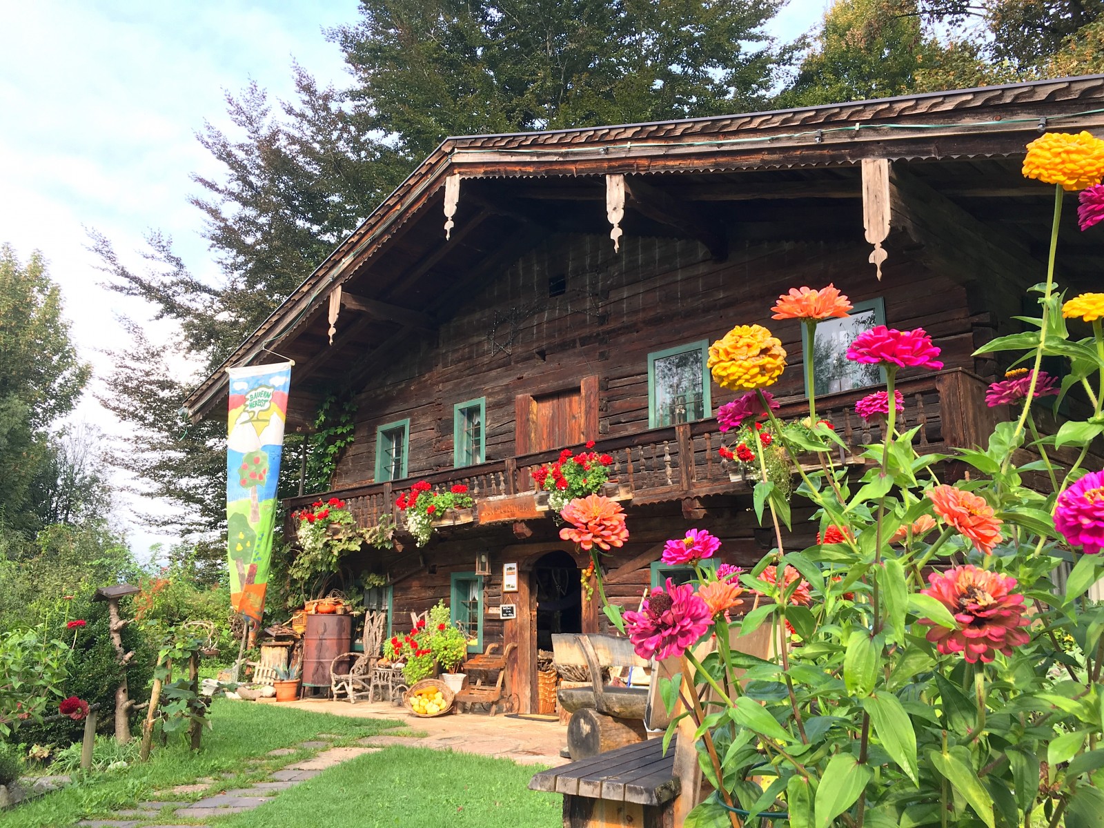 Ein rustikales Holzhaus mit bunten Blumen im Garten und einer festlichen Fahne am Eingang.