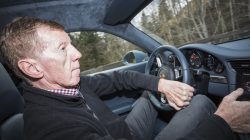 Ein Mann fährt ein Auto, hält sich am Lenkrad fest und konzentriert sich auf die Straße, während durch das Fenster Bäume zu sehen sind.