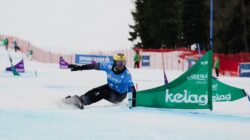 Ein Snowboard Weltmeister aus dem SalzburgerLand in blau rast um eine grüne Flagge auf einem verschneiten Slalomkurs.