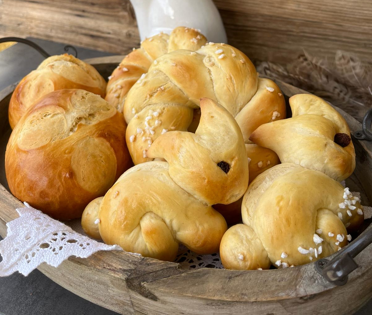 Ein Holzkorb, gefüllt mit süßen, hasenförmigen und runden Goldbrötchen, die mit Perlzucker bestreut sind.