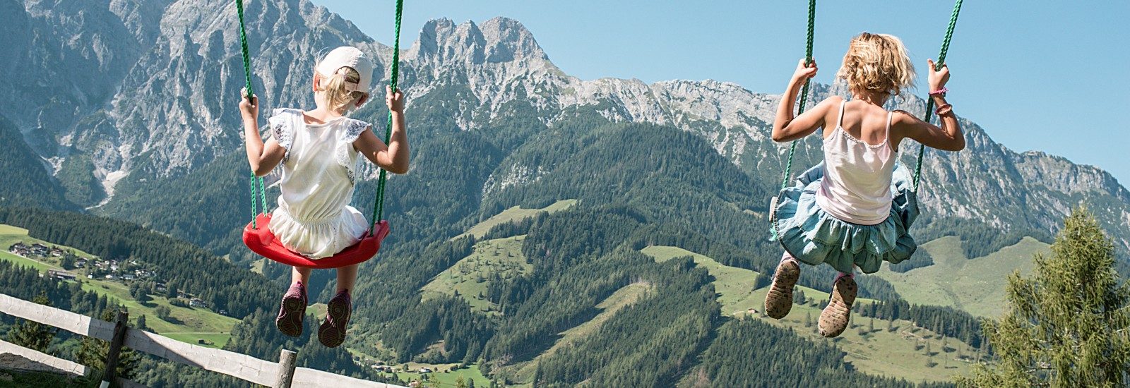 SChaukelnde Kinder vor der Aussicht auf die Bergwelt von Saalfelden Legoang