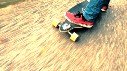 Eine Person mit roten Schuhen fährt auf einem Skateboard auf einem verschwommenen, strukturierten Weg.