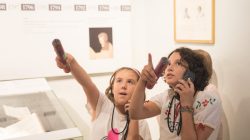 Zwei Mädchen benutzen Audioguides und zeigen auf ein Ausstellungsstück in einem Museum.