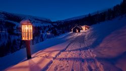 Die verschneiten Hütten leuchten in der Abenddämmerung wie gemütliche Weihnachtsmärkte, mit Laternen und Tannen am verschneiten Hang.
