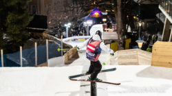 Ein Skifahrer mit Helm und nummerierter Weste rutscht bei einer nächtlichen Skiveranstaltung auf einer Schiene.