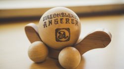 Ein Holzspielzeug mit Rädern und eingraviertem Drechsler Angerer auf einer runden zentralen Kugel.