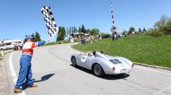 Eine Person schwenkt die Zielflagge, während sich ein Oldtimer an einem sonnigen Tag der Ziellinie nähert.