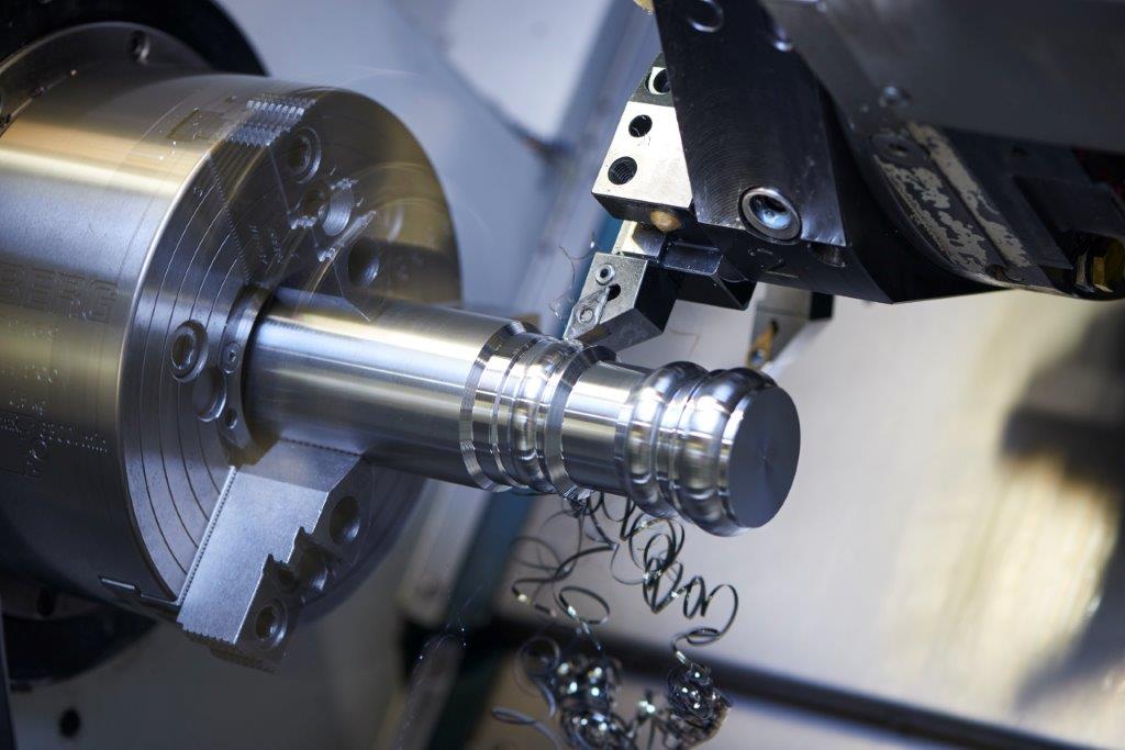 Eine CNC-Drehmaschine verbindet Tradition mit Kunsthandwerk, indem sie einen Metallzylinder präzise formt, während die Späne davonfliegen.