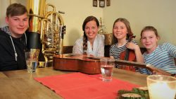 Vier lächelnde Menschen, darunter Anna-Cäcilia Pföß, sitzen an einem Tisch mit Instrumenten und Getränken in einem festlichen Raum.