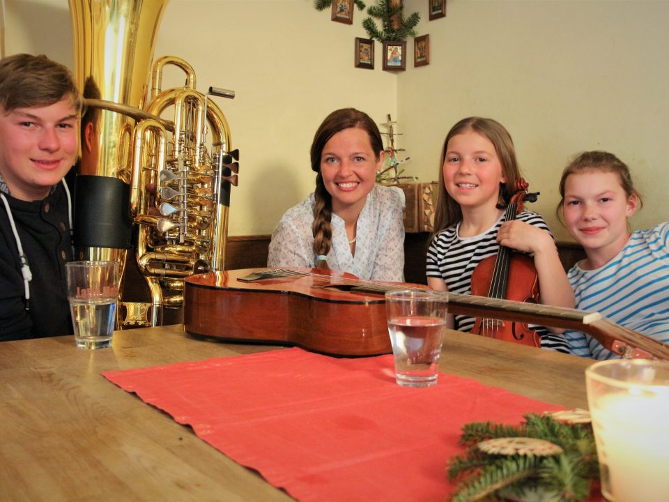 Vier lächelnde Menschen, darunter Anna-Cäcilia Pföß, sitzen an einem Tisch mit Instrumenten und Getränken in einem festlichen Raum.