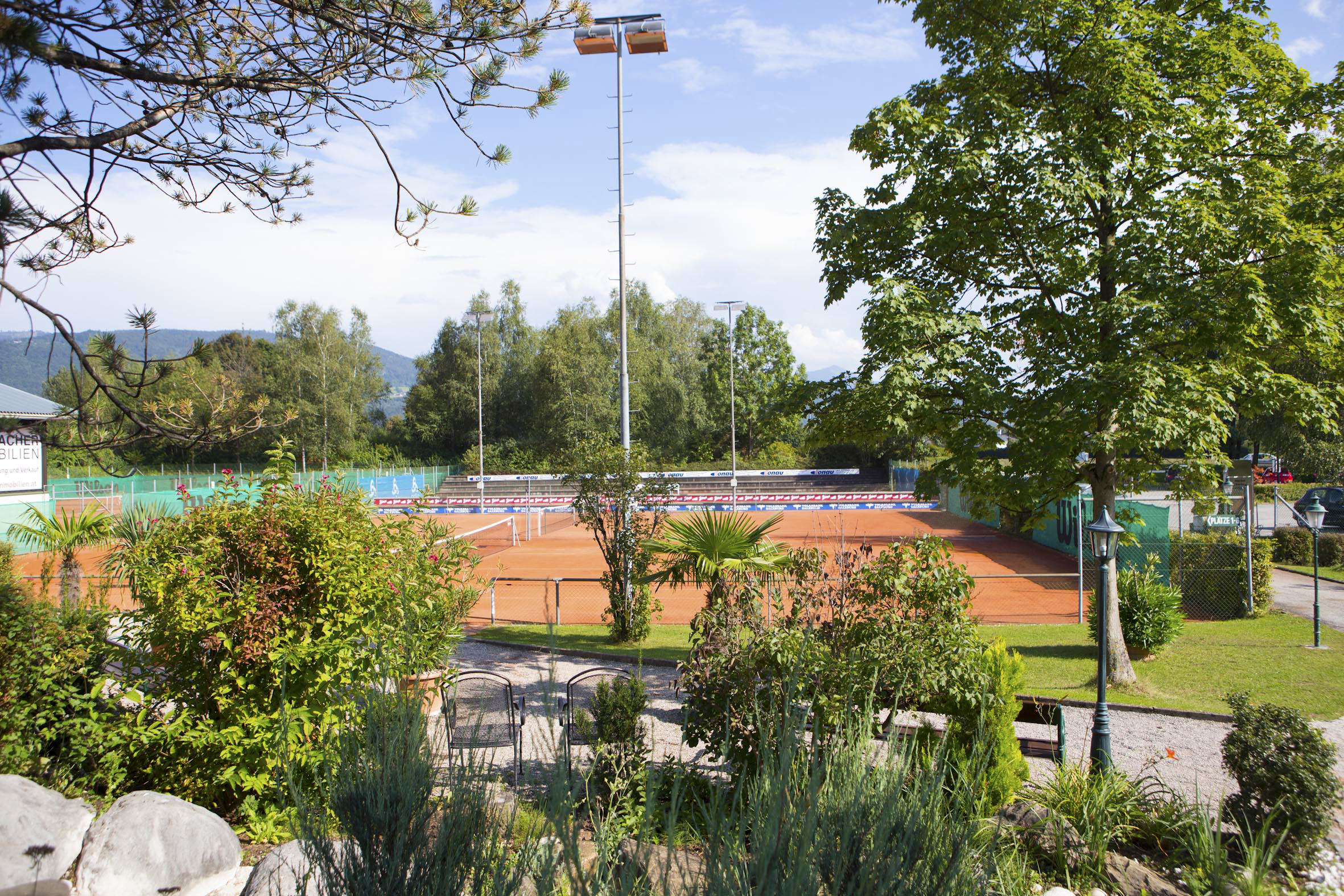 Tennisplatz im Freien, umgeben von Grün und Bäumen, ideal für einen sonnigen Tennistag.