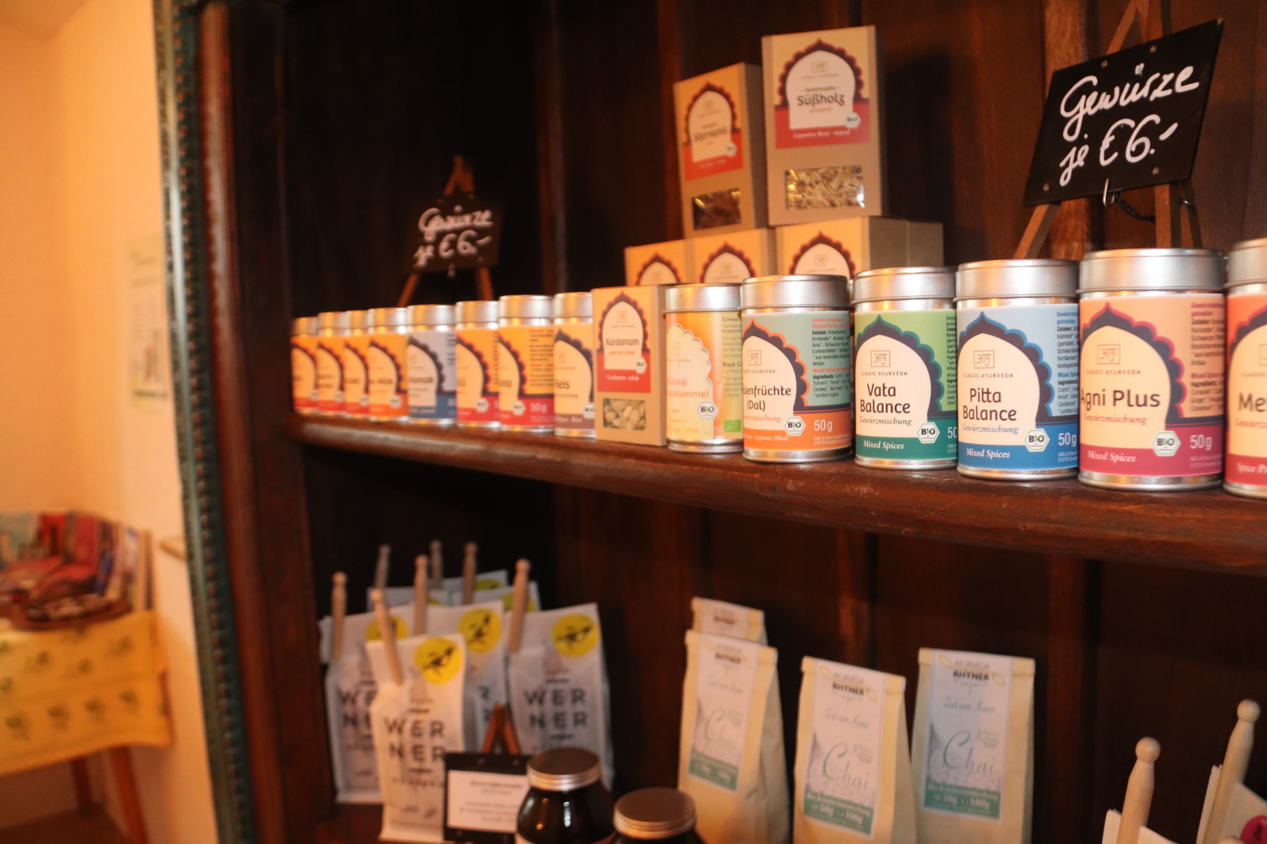 Bunte Gewürzbehälter auf Holzregalen in Die Tauglerei, einem Zentrum für Ayurveda und vieles mehr.