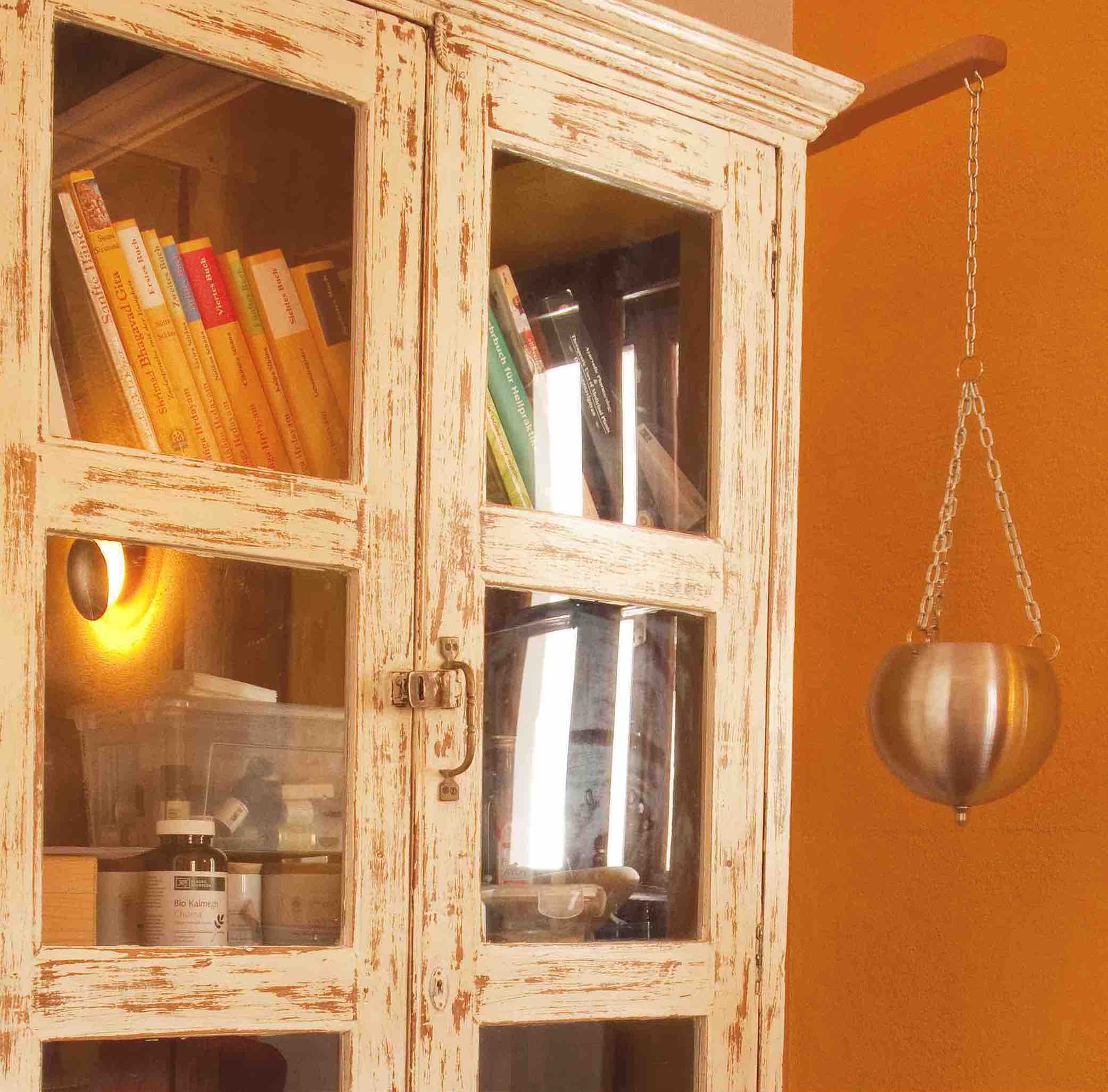 Distressed white cabinet with glass doors, books inside, near Die Tauglerei ist ein Zentrum für Ayurveda und vieles mehr.