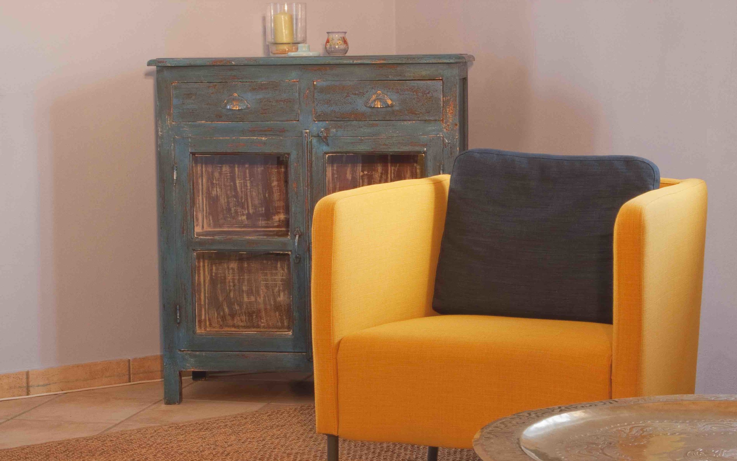 Ein gelber Sessel und ein blauer Schrank verleihen einem gemütlichen Raum in der Tauglerei, Zentrum für Ayurveda und mehr, Gemütlichkeit.