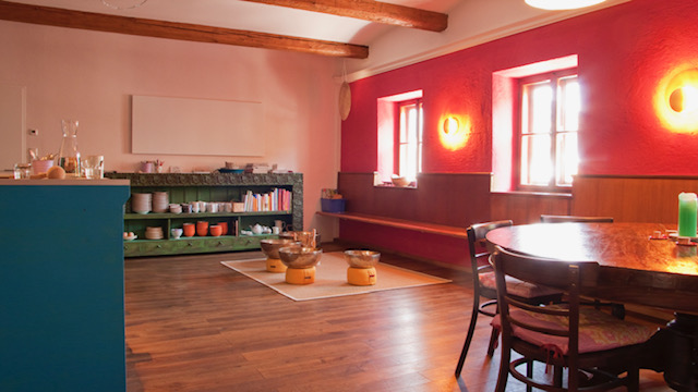 Bunter Essbereich in der Tauglerei, einem Zentrum für Ayurveda und vieles mehr, mit Sonnenlicht und offenen Regalen.