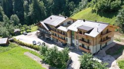 Luftaufnahme eines modernen Bike-Hotels im Saalachtal, das inmitten von Bäumen und Grünflächen an einem Hang liegt.