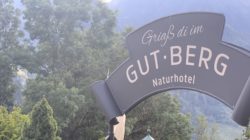 Eingangsschild von Gut Berg Naturhotel mit Bäumen und Bergen im Hintergrund.