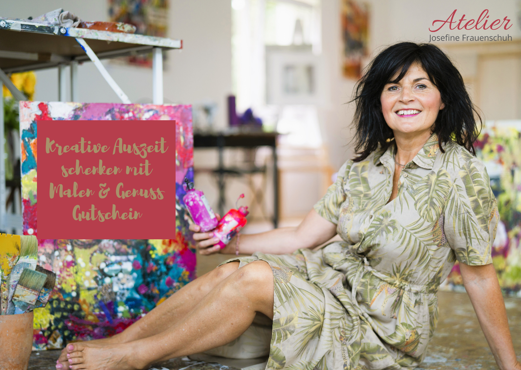 Lächelnde Frau sitzt auf dem Boden eines Ateliers und hält einen gemalten Pinsel neben einer bunten Leinwand; der Text wirbt für einen Kunstgutschein.