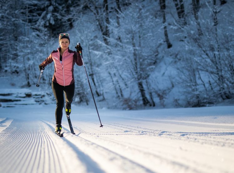 Person beim Langlaufen auf einer präparierten Schneepiste mit Bäumen im Hintergrund.
