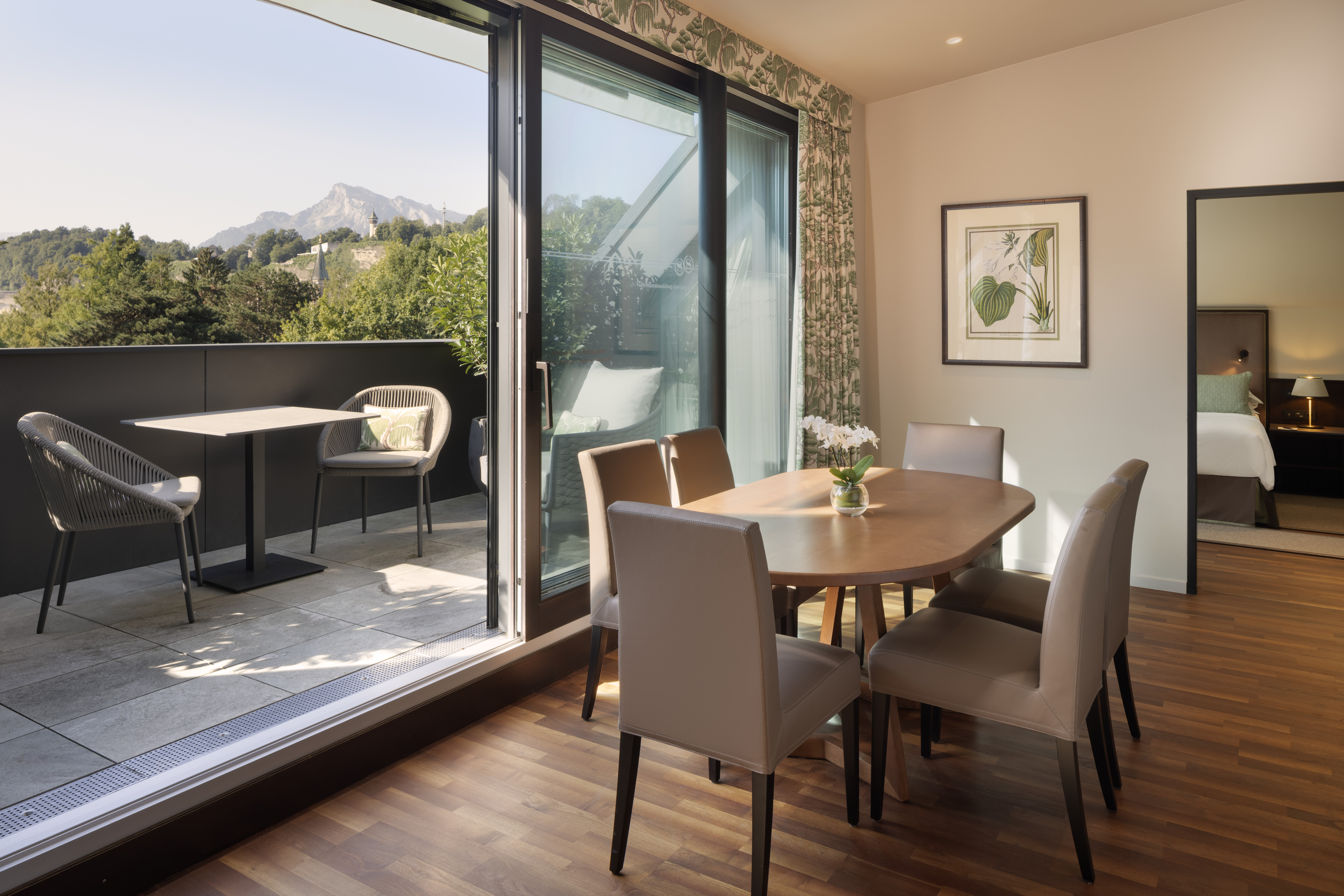 Essbereich mit sechs Stühlen, offen zur Terrasse des Sheraton Grand Salzburg, mit Blick auf die Berge und Bäume.