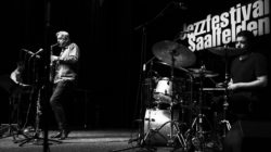 Schwarz-Weiß-Foto einer Jazzband auf der Bühne des Jazzfestivals Saalfelden, mit Schlagzeug und Saxophon.
