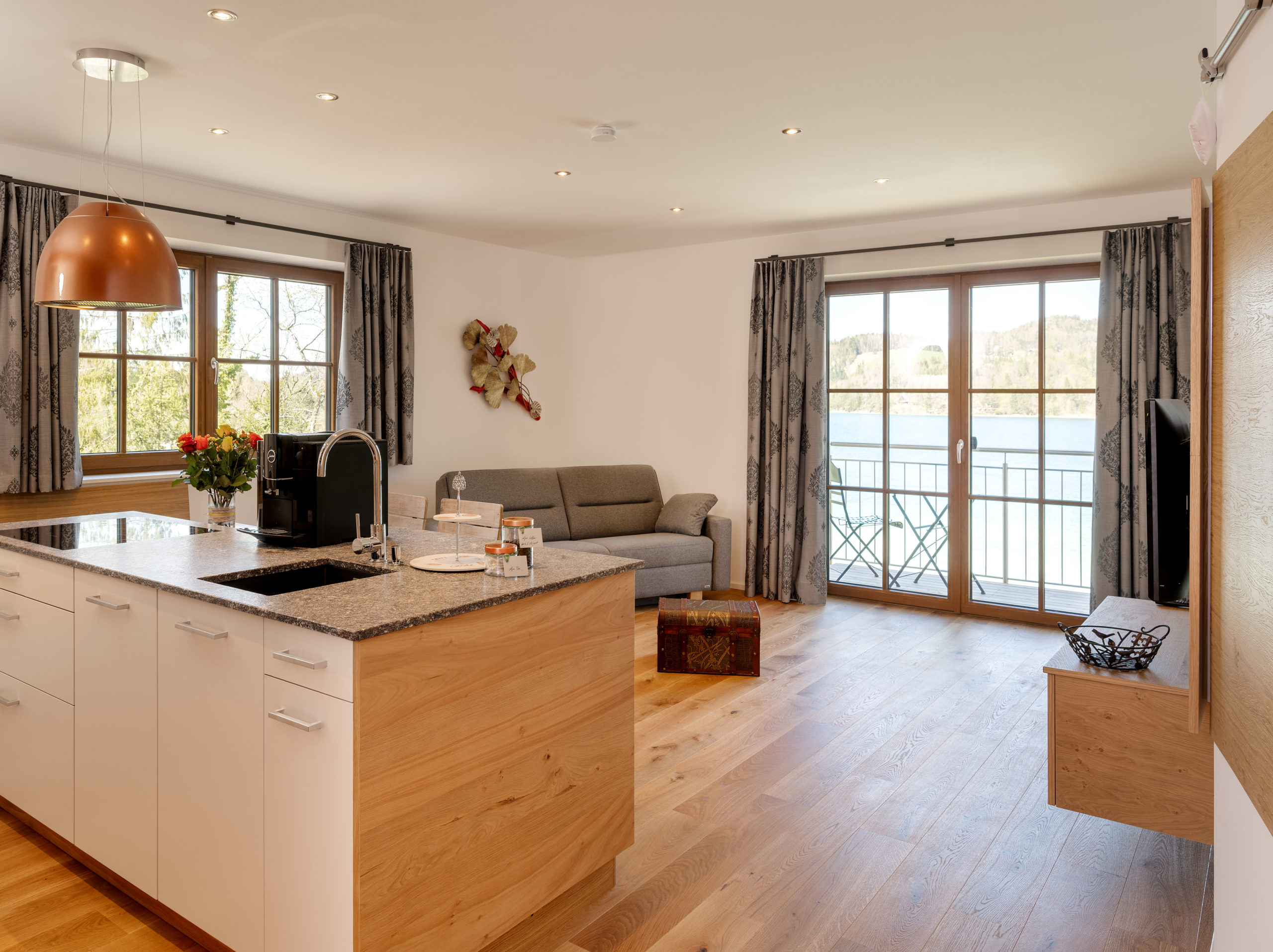 Moderne offene Küche und Wohnzimmer mit Holzböden, großen Fenstern und Brunnwirt-Seeblick.