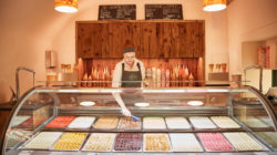 Eine lächelnde Bedienung schöpft Eis hinter einer Glasvitrine mit bunten Geschmacksrichtungen in einer Eisdiele.