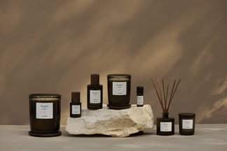 Eine Sammlung von Manufaktur-Kerzen und Diffusoren auf einem Stein mit neutralem Hintergrund.