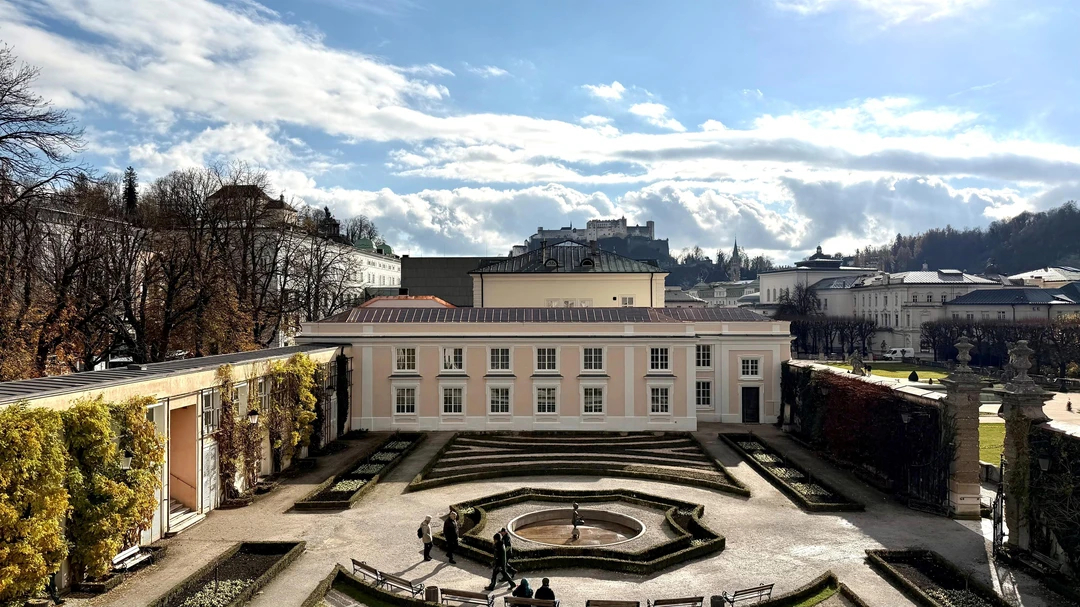 Ein rechteckiger Hof mit einem zentralen Springbrunnen, umgeben von G&auml;rten, Geb&auml;uden und einer entfernten Burg.
