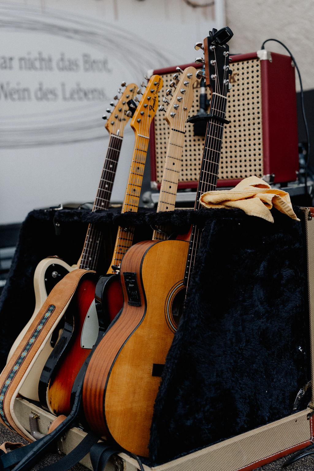 Vier Gitarren in einem schwarzen St&auml;nder neben einem Verst&auml;rker, &uuml;ber dem ein gelbes Tuch drapiert ist.