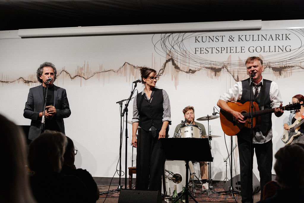 Vier Musiker stehen auf der B&uuml;hne, einer singt, einer spielt Gitarre, dahinter spielen ein Schlagzeuger und ein Bassist.