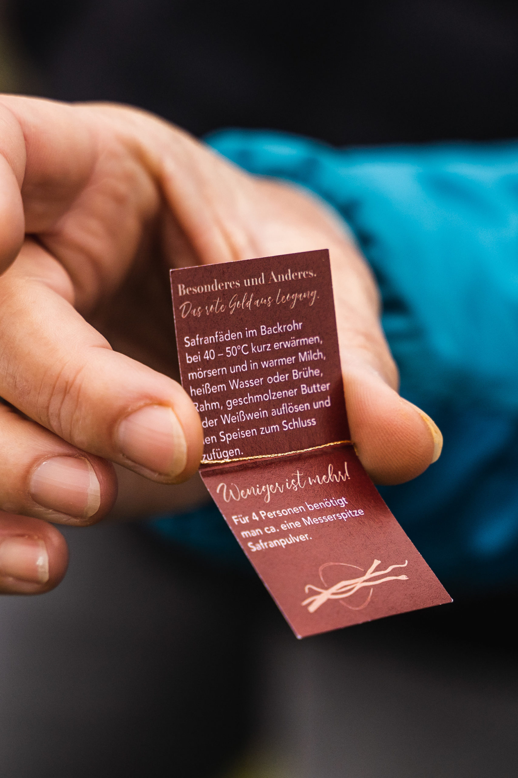 Eine Hand hält eine gefaltete Karte mit deutschem Text über Safran und Rezeptanweisungen.