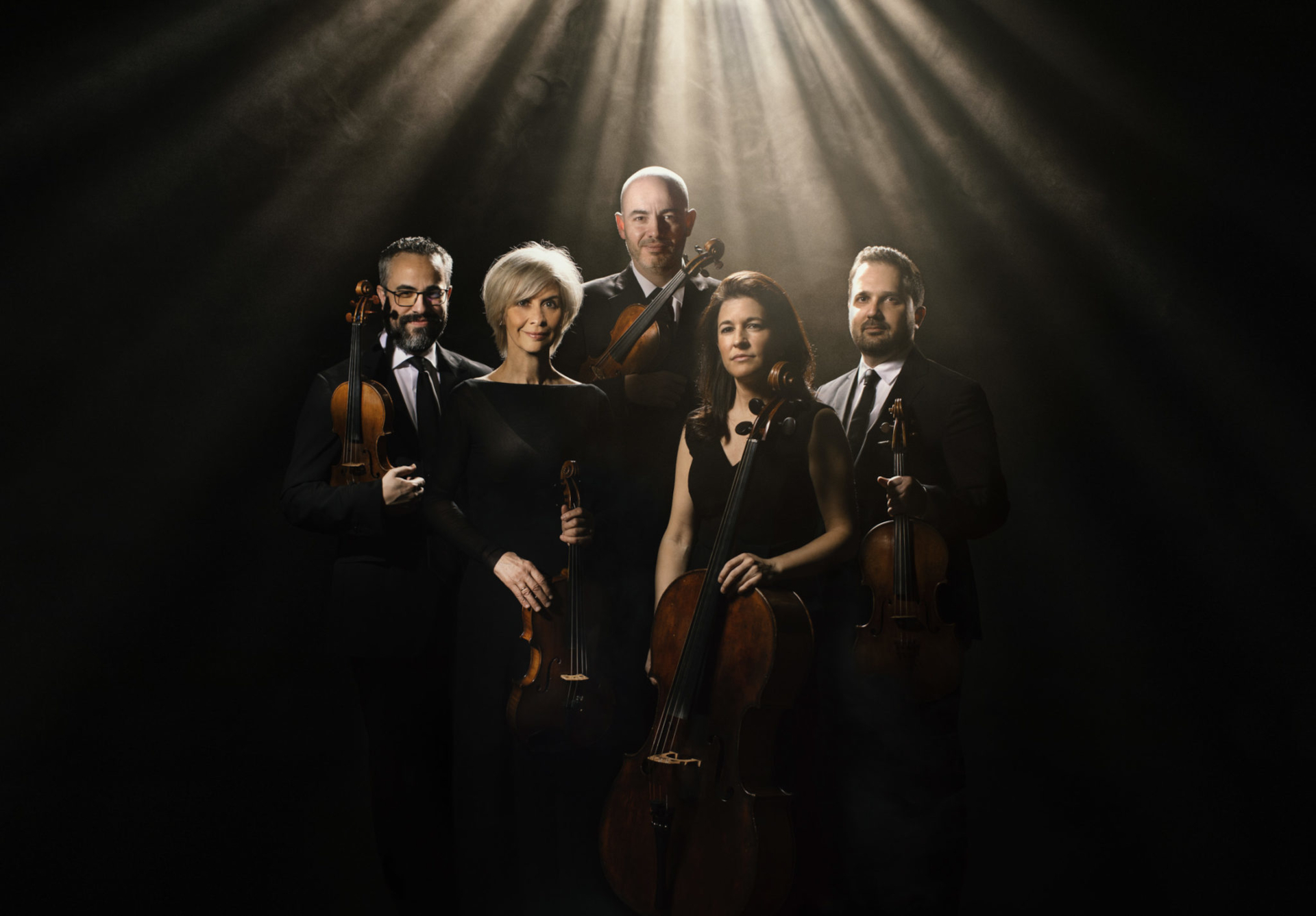 Fünf klassische Musiker in formeller schwarzer Kleidung halten Streichinstrumente in der Hand und sind bereit, unter dramatischer Beleuchtung Mozart zu spielen.